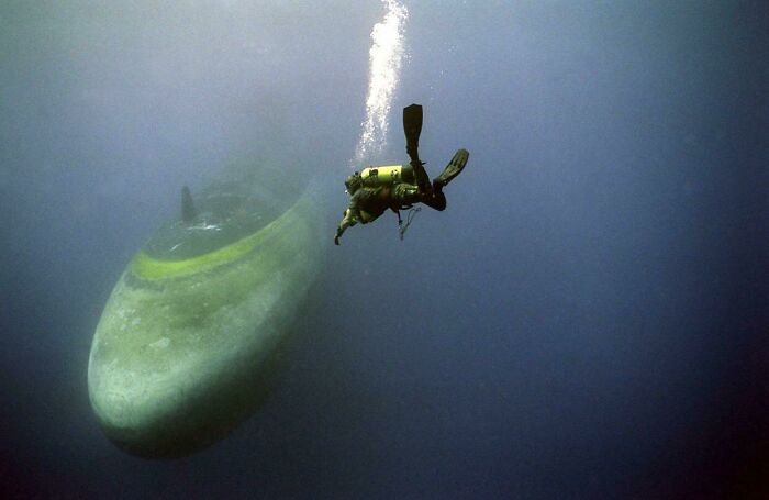 Diver swimming near a massive submarine underwater, illustrating the fear of deep waters and triggering thalassophobia.