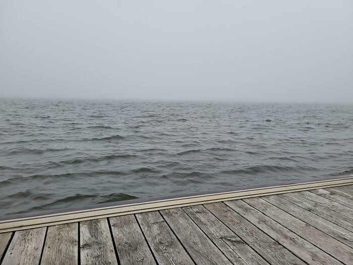 Wooden dock overlooking dark, foggy ocean waves evoking a sense of thalassophobia and fear of deep waters.