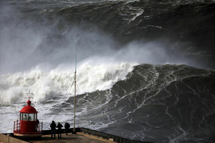 Massive dark waves crash near a small red lighthouse, illustrating intense thalassophobia fear of deep waters.