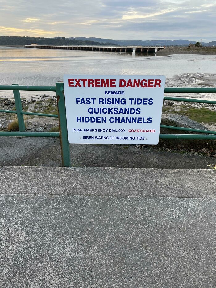 Warning sign on waterfront about fast rising tides, quicksands, and hidden channels triggering thalassophobia fears.