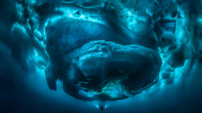 Underwater view of a diver exploring deep waters beneath a massive ice formation triggering thalassophobia fears.