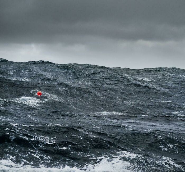 Stormy dark ocean waves with a small red buoy, evoking thalassophobia and fear of deep waters under a gloomy sky.