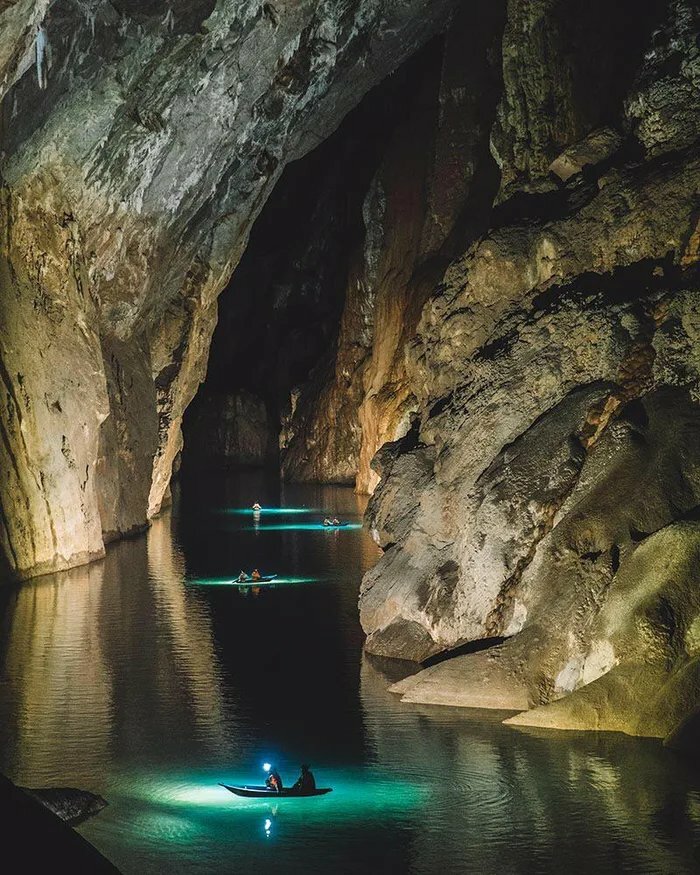 Boats with glowing lights navigate deep waters inside a large cave, illustrating the fear of deep waters with eerie surroundings.
