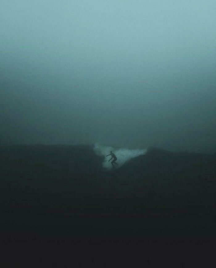 Surfer barely visible in dark deep waters, evoking strong feelings of thalassophobia and fear of deep water.