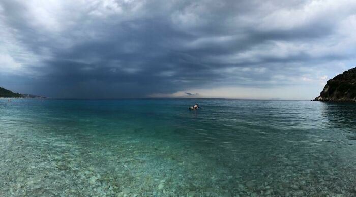 Stormy sky over deep blue water with a lone swimmer, evoking strong feelings of thalassophobia and fear of deep waters.
