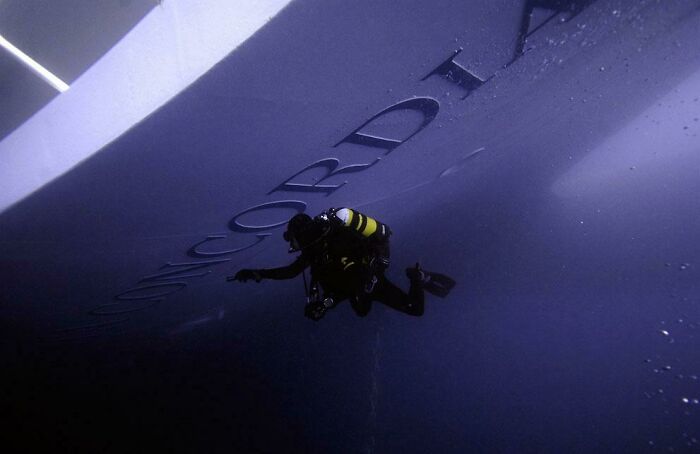 Scuba diver exploring deep dark waters near a large shipwreck, triggering thalassophobia and fear of deep waters.