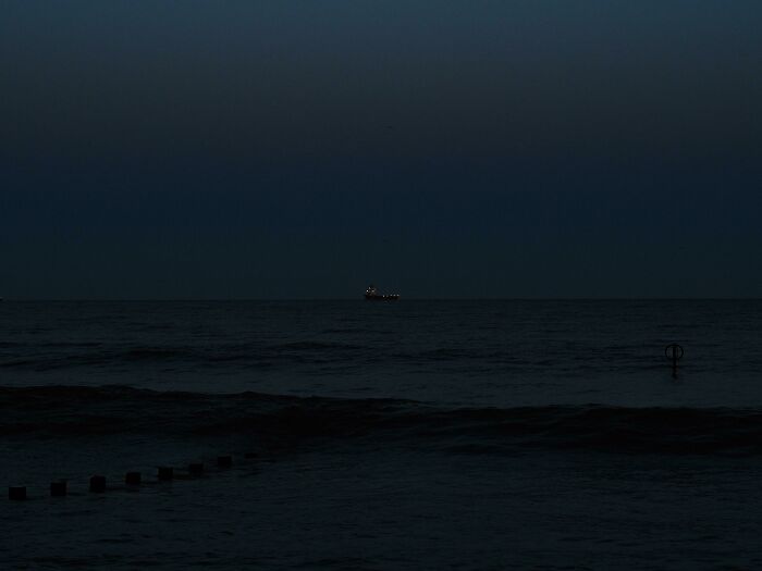 Dark deep waters at night with a distant ship, evoking feelings linked to thalassophobia and fear of open sea.