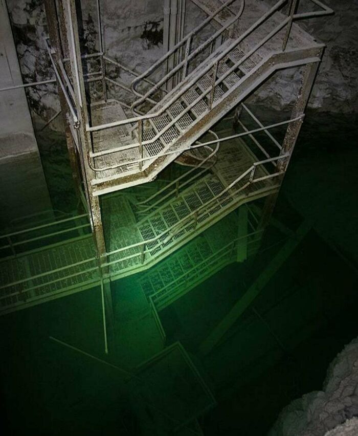 Rusty metal stairway descending into dark green water, evoking fear of deep waters and triggering thalassophobia.