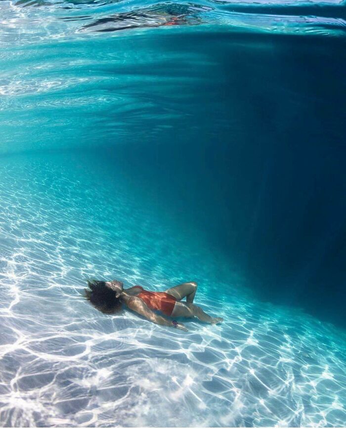 Person lying on the ocean floor near dark deep waters, evoking strong feelings of thalassophobia and fear of deep water.