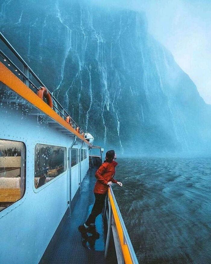 Person in red jacket on a boat near deep, dark waters and towering cliffs, evoking thalassophobia fear of deep waters.
