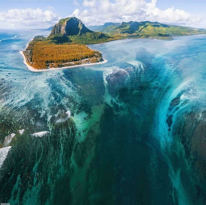 Aerial view of a coastline featuring a deep underwater drop-off and clear ocean waters triggering thalassophobia.