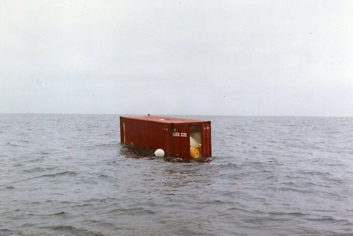 A partially submerged red shipping container floating in deep waters, triggering thalassophobia fears.
