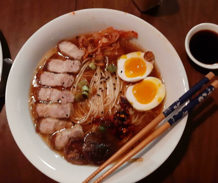 Bowl of nearly perfect ramen with soft-boiled eggs, sliced pork, noodles, and spices, presented beautifully with chopsticks.