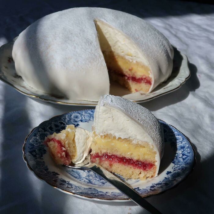 Slice of nearly perfect layered cake with white frosting and raspberry filling on a decorative plate in natural light.