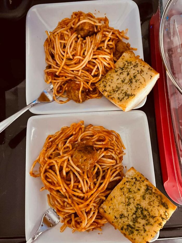 Two plates of nearly perfect spaghetti with meatballs and garlic bread served with forks on a dark table.