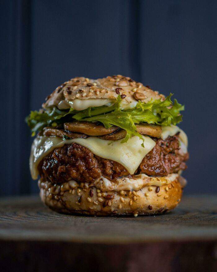 Close-up of a nearly perfect burger with melted cheese, lettuce, and mushrooms on a seeded bun, showcasing beautiful food presentation.