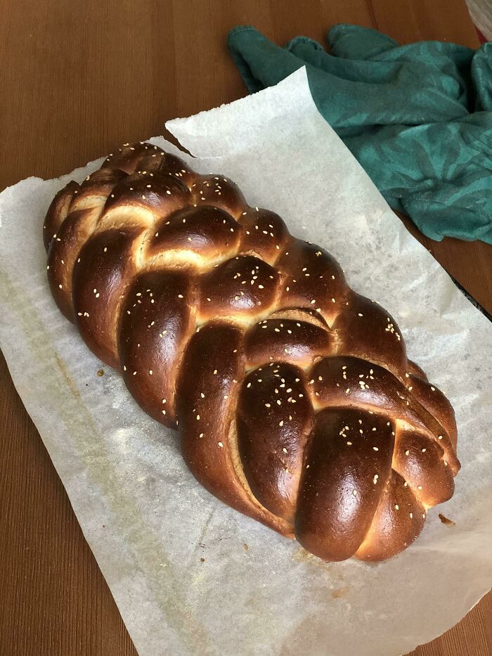 Freshly baked, nearly perfect braided bread with a shiny crust and sesame seeds on parchment paper on a wooden table