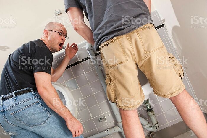 Two men in a restroom, one appears surprised. Weird stock image capturing an unusual moment in a bathroom setting.