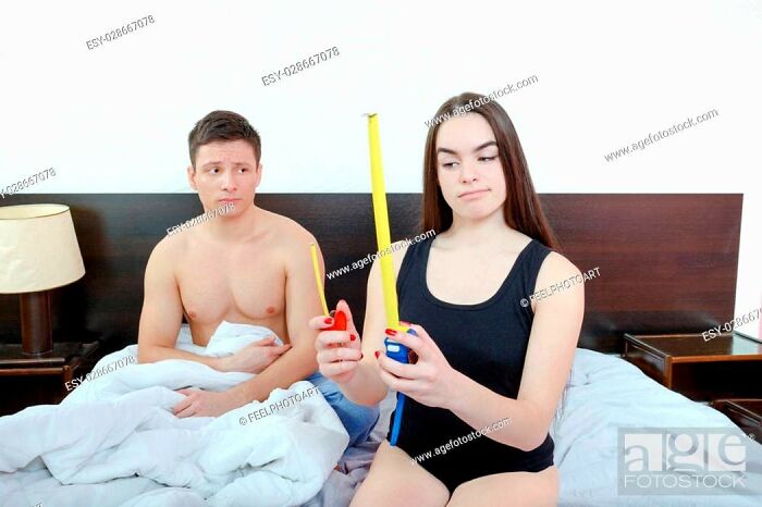 A woman measures with a tape measure next to a surprised man in bed, illustrating weird stock images.