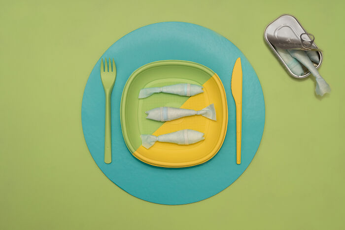 Plate with plastic-wrapped items shaped like fish with a fork and knife, highlighting environmental problems of the Earth.