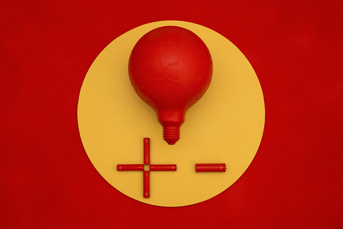 Red light bulb and batteries arranged as a plus and minus sign on a yellow plate highlighting Earth problems.