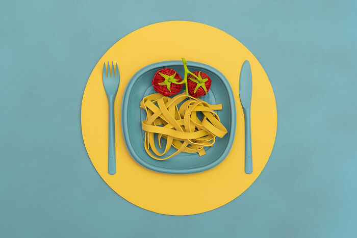 Blue plate with pasta and tomatoes arranged on a yellow placemat, symbolizing earth problems served on a plate.
