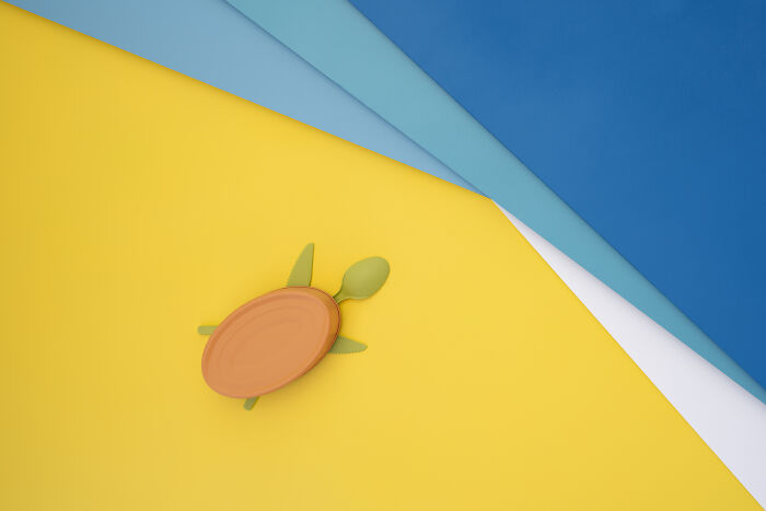 Minimalist food art of a turtle made with a plate and cutlery, symbolizing environmental problems of the Earth on a colorful background.