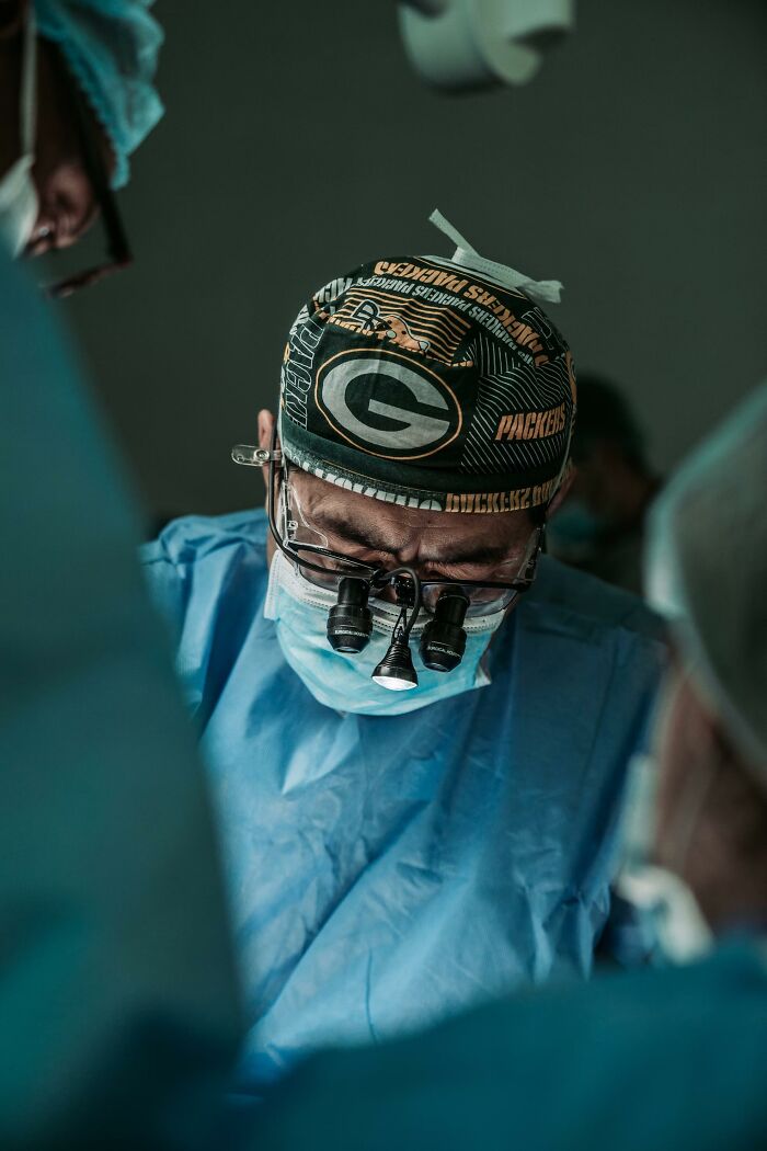 Surgeon wearing surgical cap and magnifying glasses performing surgery in operating room with focused attention.
