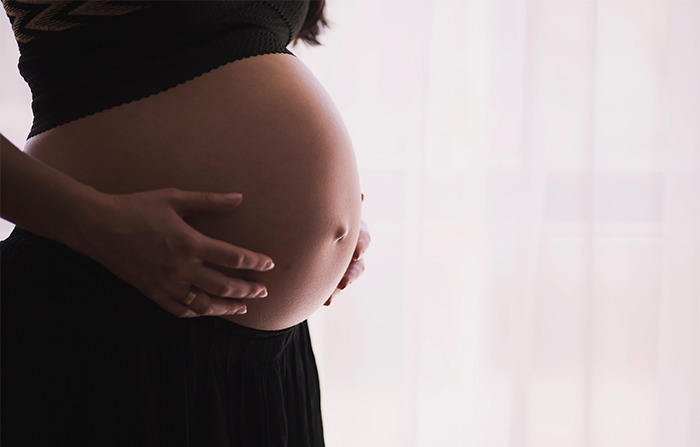 Pregnant woman holding her belly in soft natural light illustrating disturbing things about human bodies.