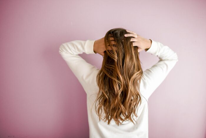 Woman with long brown hair wearing white sweater, facing a pink wall, illustrating disturbing things about human bodies concept.