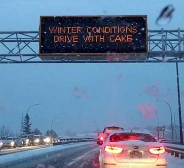 Highway electronic sign showing a hilarious and absurd winter driving message during snowfall.