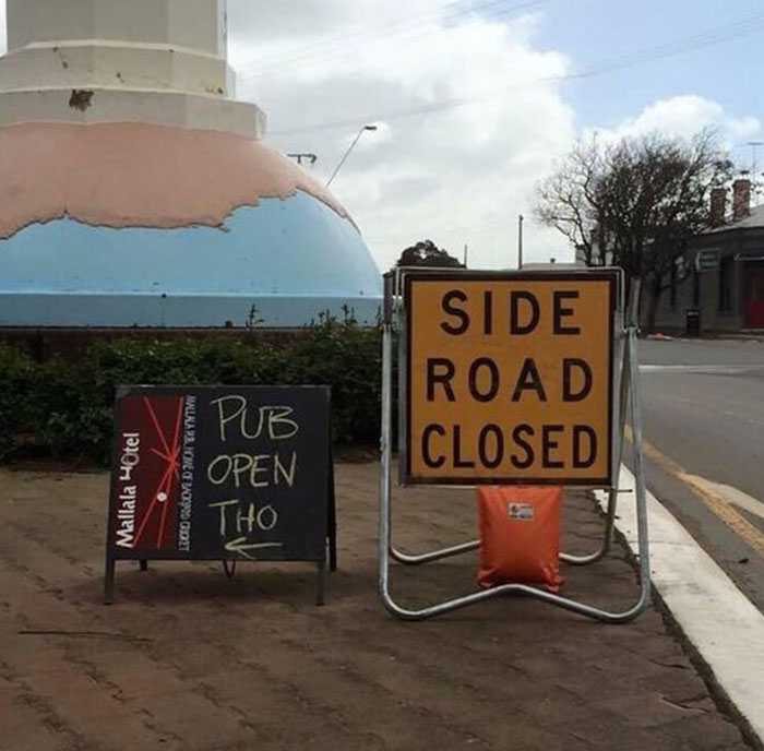 Side road closed sign next to a humorous chalkboard sign saying pub open tho, highlighting hilarious and absurd signs.