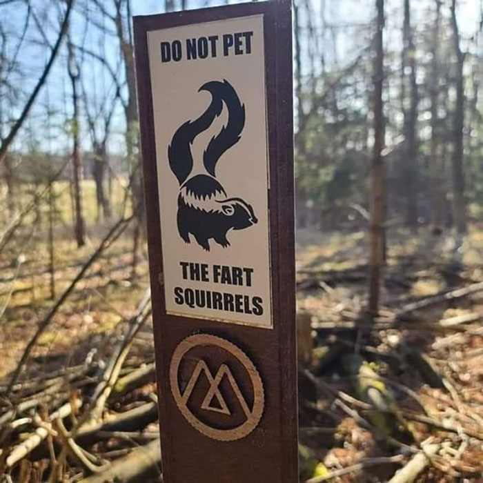 Hilarious and absurd sign warning not to pet the fart squirrels posted on a wooden post in the forest.