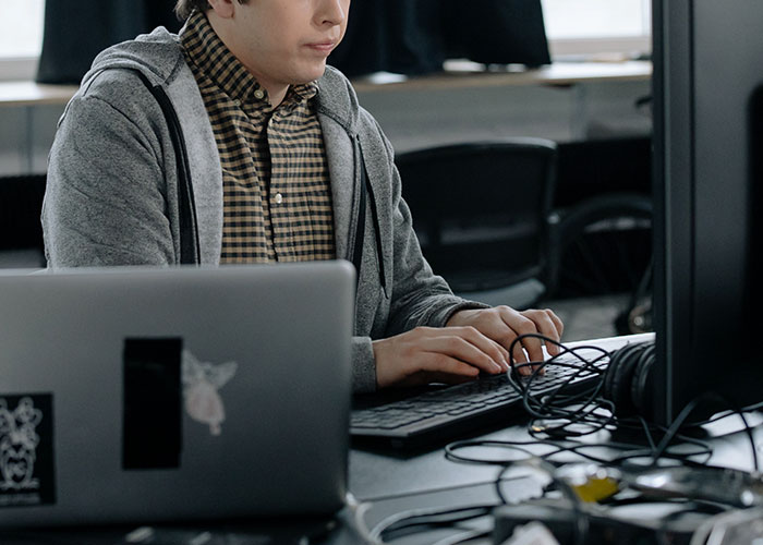 Person working at a computer, symbolizing how they became millionaires, wearing a gray hoodie and checkered shirt.