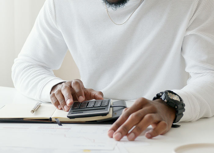 Person using a calculator, analyzing financial documents, symbolizing millionaire strategies.