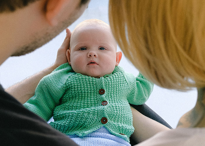 Parents holding a baby in a green sweater.