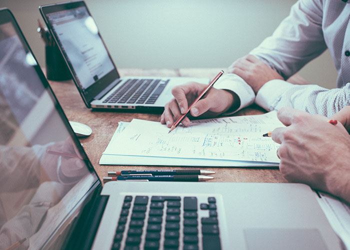 Two people discussing financial strategies at a desk with laptops and notes, aiming to become millionaires.