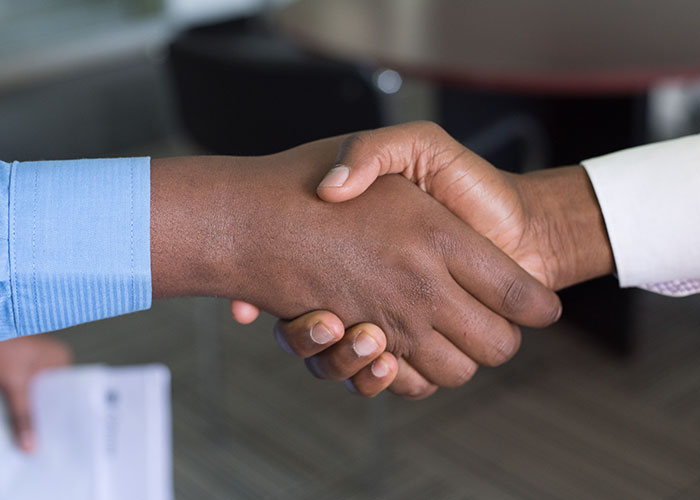 Two people shaking hands, symbolizing agreement or partnership, related to becoming millionaires.