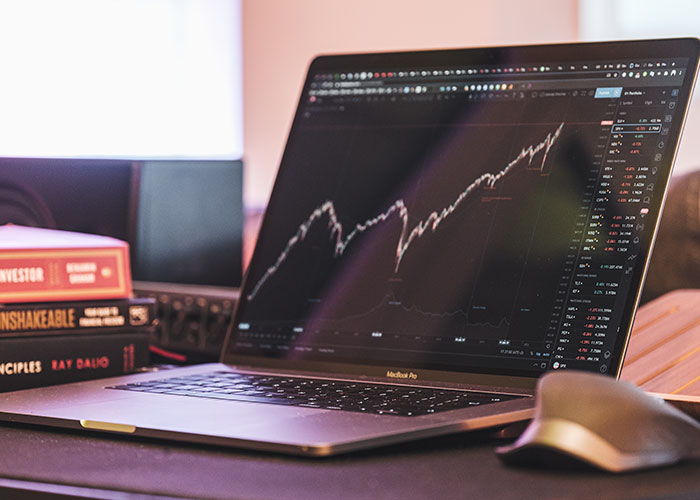 Laptop displaying stock market trends, a tool vital for becoming millionaires, alongside investment books.