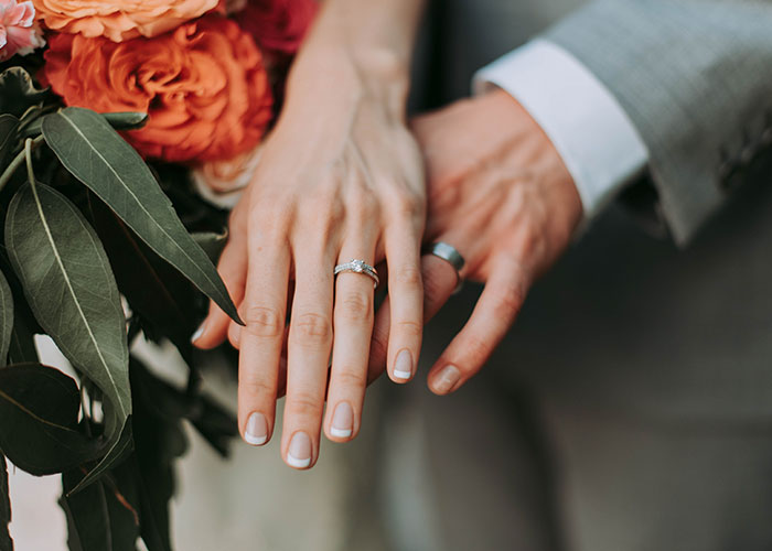 Close-up of a couple's hands with wedding rings, holding a bouquet, symbolizing partnership in becoming millionaires.