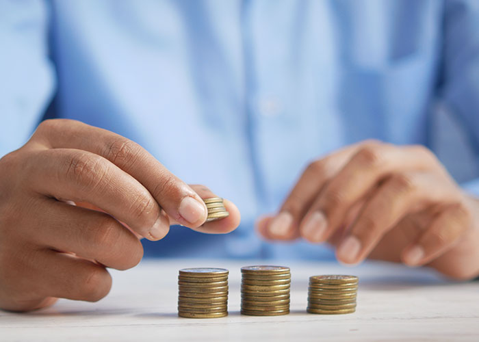 Person stacking coins on a table, illustrating a pathway to becoming a millionaire.