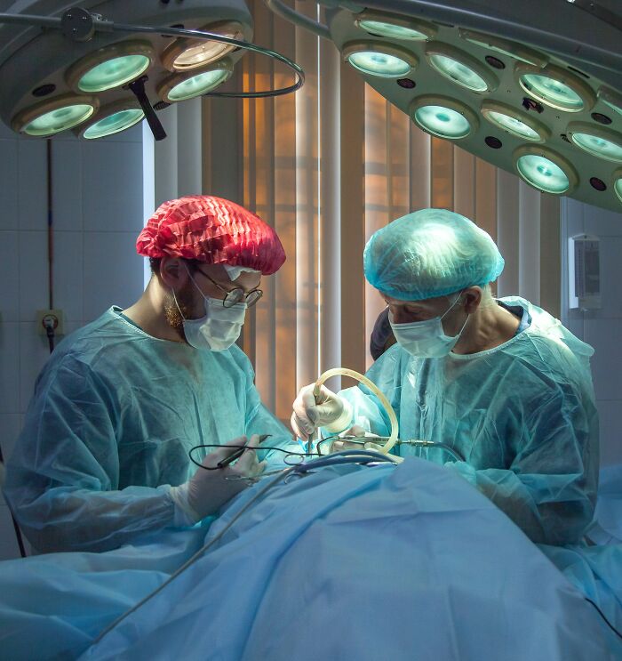 Two surgeons in surgical gowns and masks performing a delicate operation under bright surgical lights in an operating room.