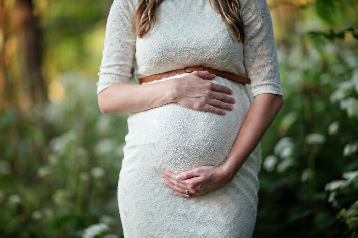 Pregnant woman in a white lace dress gently holding her belly, illustrating fascinating aspects of human bodies.