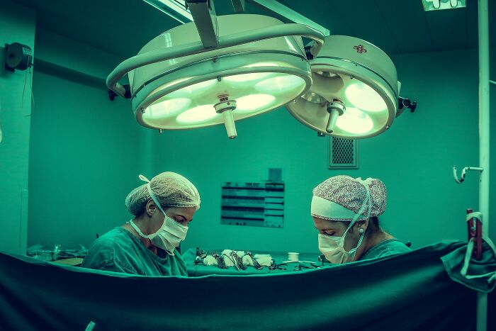 Two surgeons in an operating room performing surgery under bright surgical lights, highlighting disturbing things about human bodies.