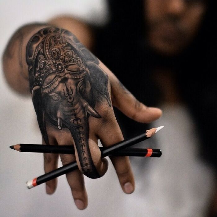 Hand with intricate tattoo of an elephant holding pencils, showcasing genius tattoos.