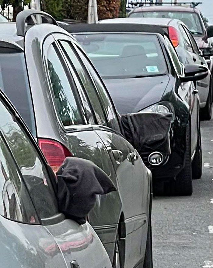 ¿Qué es esta cosa? - Dos coches aparcados en una calle, ambos parecen tener camisetas (o algún tipo de material) sobre los retrovisores, pero sólo en el lado que da a la carretera