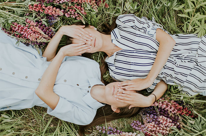 Two woman laying on grass covering each others hands 
