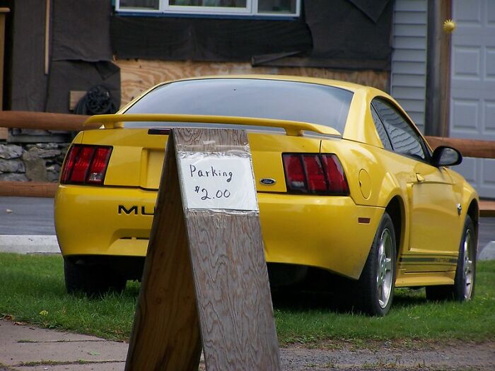 Yellow car parked near a handwritten parking note offering spots for two dollars on a wooden signboard.