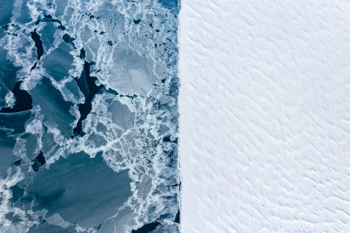 Aerial view showing contrast between frozen ocean ice and a snow-covered landscape, capturing Earth's diverse natural beauty.