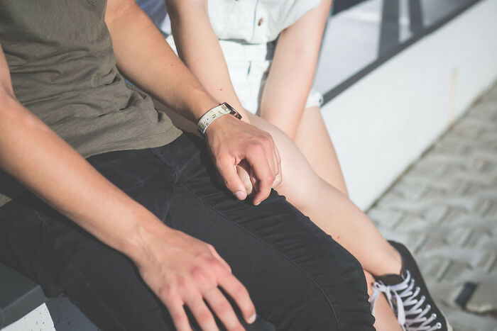 Close-up of two people holding hands while sitting outdoors, illustrating unexpected moments like startling windshield notes found.